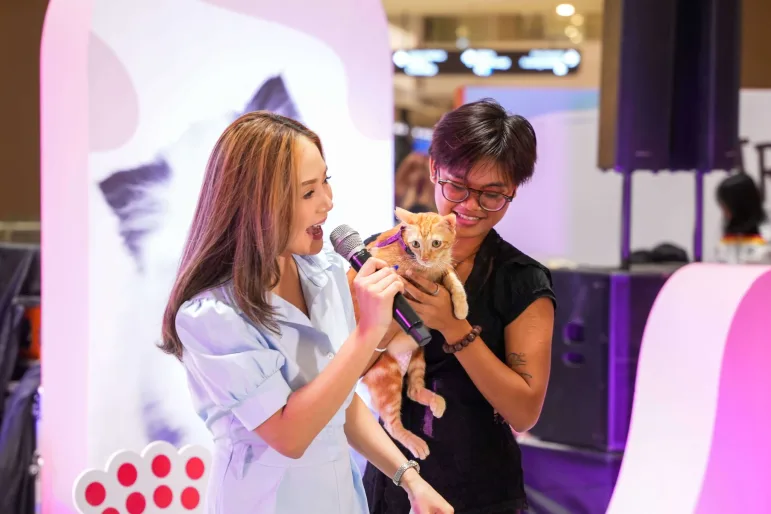 An owner holds their kitten on the stage area while talking to a host of Puppy & Kitten Con